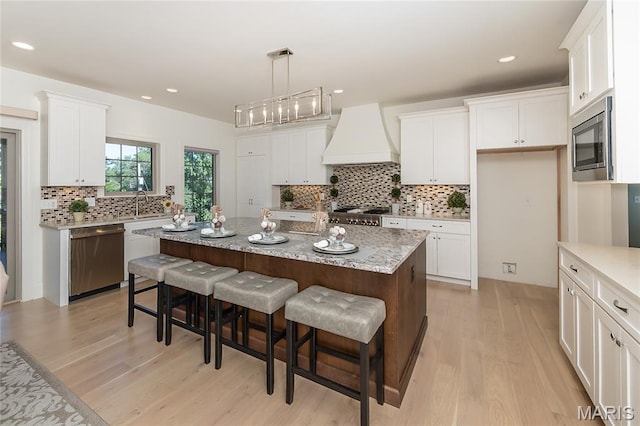 111 N Mosley Rd, Saint Louis, MO 63141 - kitchen with appliances with stainless steel finishes, custom range hood, light wood-style floors, backsplash, and white cabinetry
