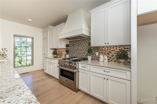 111 N Mosley Rd, Saint Louis, MO 63141 - kitchen featuring high end stove, custom range hood, light wood finished floors, tasteful backsplash, and white cabinets