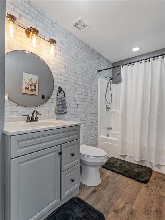 109 N 7th St, Owensville, MO 65066 - bathroom with vanity, shower / bath combination with curtain, brick wall, toilet, and wood finished floors