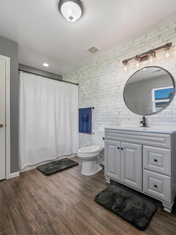 109 N 7th St, Owensville, MO 65066 - bathroom featuring brick wall, vanity, toilet, wood finished floors, and curtained shower