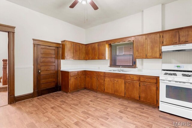 207 Voss Pl, Belleville, IL 62220 - kitchen featuring white range with gas cooktop, under cabinet range hood, a sink, brown cabinets, and a wainscoted wall