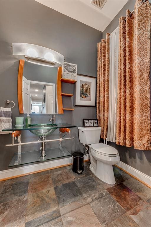 2628 Indiana Ave, Saint Louis, MO 63118 - bathroom with baseboards, toilet, stone finish flooring, and a sink