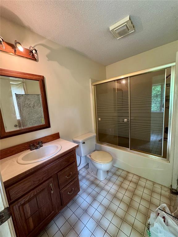 10321 Old 79, Hannibal, MO 63401 - full bath with toilet, vanity, a textured ceiling, shower / bath combination with glass door, and tile patterned flooring
