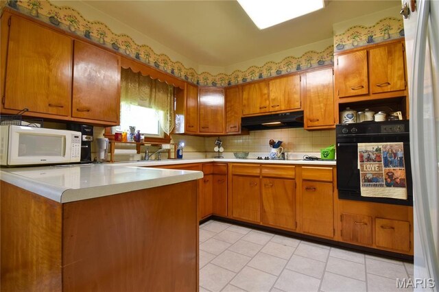 411 S Walnut St, Mount Olive, IL 62069 - kitchen featuring white microwave, black oven, under cabinet range hood, brown cabinetry, and light countertops