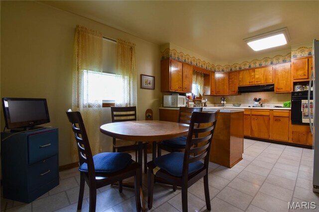 411 S Walnut St, Mount Olive, IL 62069 - kitchen featuring under cabinet range hood, brown cabinetry, white microwave, backsplash, and light countertops