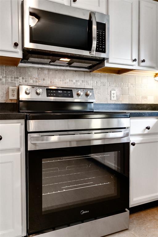 2447 Hartland Ave, Sycamore Hills, MO 63114 - kitchen featuring appliances with stainless steel finishes, dark countertops, backsplash, and white cabinetry