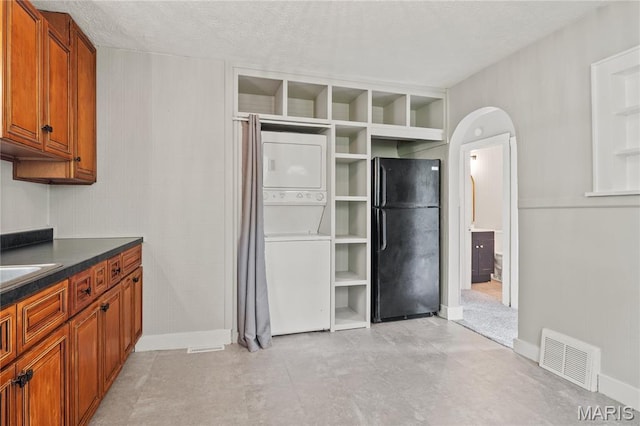 233 Oconnell St, Cape Girardeau, MO 63701 - kitchen with freestanding refrigerator, stacked washer / drying machine, brown cabinets, dark countertops, and arched walkways