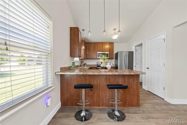 119 Hidden Bluffs Dr, Lake St Louis, MO 63367 - kitchen featuring appliances with stainless steel finishes, lofted ceiling, light wood-style floors, brown cabinets, and a peninsula