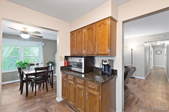 1001 Windstream Dr Unit 32, Saint Peters, MO 63376 - kitchen with stainless steel microwave, wood finished floors, brown cabinetry, dark stone countertops, and baseboards