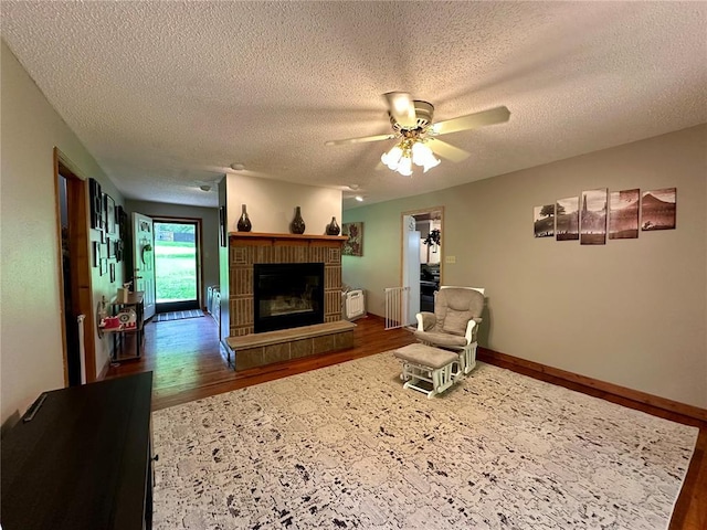 12185 Oak Meadow Dr, Rolla, MO 65401 - living room featuring wood finished floors, a textured ceiling, ceiling fan, and a glass covered fireplace