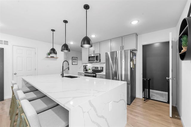369 Tiber Pl, Saint Charles, MO 63301 - kitchen with appliances with stainless steel finishes, a sink, light stone counters, light wood-style floors, and a center island with sink