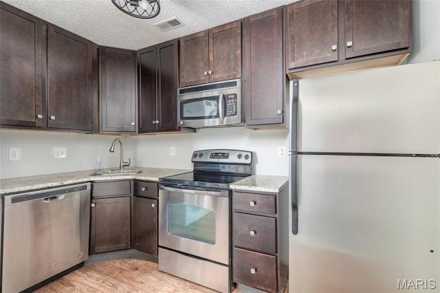 1447 Oriole Pl, Brentwood, MO 63144 - kitchen with appliances with stainless steel finishes, dark brown cabinets, a sink, light wood finished floors, and a textured ceiling