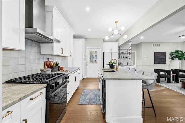 317 Greeley Ave, Webster Groves, MO 63119 - kitchen with wall chimney exhaust hood, black range with gas stovetop, a breakfast bar area, light stone countertops, and a chandelier