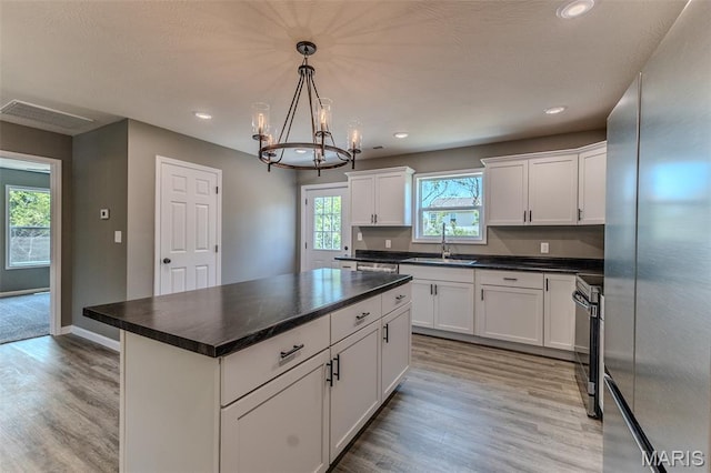 1223 Utah St, Lebanon, MO 65536 - kitchen with appliances with stainless steel finishes, a sink, white cabinets, a chandelier, and light wood finished floors