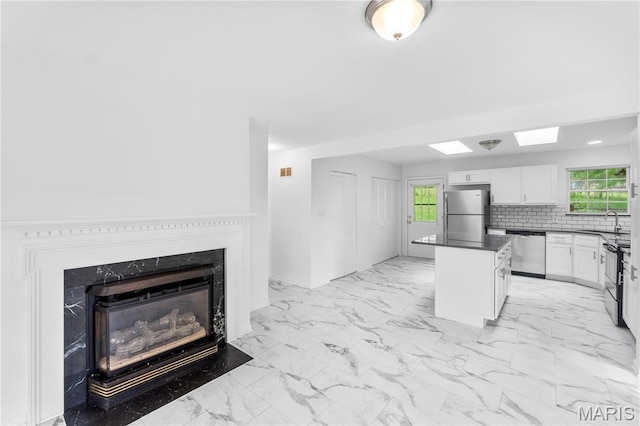 10735 Wurdack Ave, Saint Louis, MO 63114 - kitchen featuring appliances with stainless steel finishes, light marble finish floors, dark countertops, white cabinetry, and a kitchen island