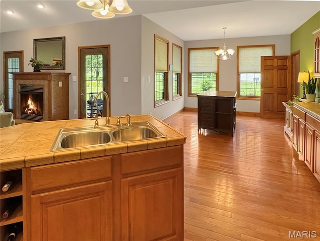 495 Oak Field Ct, Washington, MO 63090 - kitchen featuring a chandelier, a sink, light wood finished floors, a warm lit fireplace, and pendant lighting