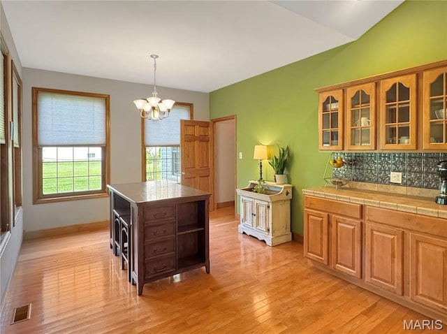 495 Oak Field Ct, Washington, MO 63090 - kitchen with light wood-style floors, a chandelier, glass insert cabinets, backsplash, and pendant lighting