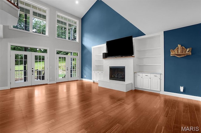 17917 Rosemar Ln, Wildwood, MO 63038 - unfurnished living room with french doors, a glass covered fireplace, wood finished floors, a towering ceiling, and built in features
