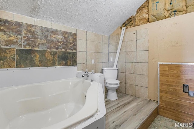 503 Newberry St, Fredericktown, MO 63645 - bathroom featuring tile walls, toilet, a garden tub, a textured ceiling, and wood finished floors