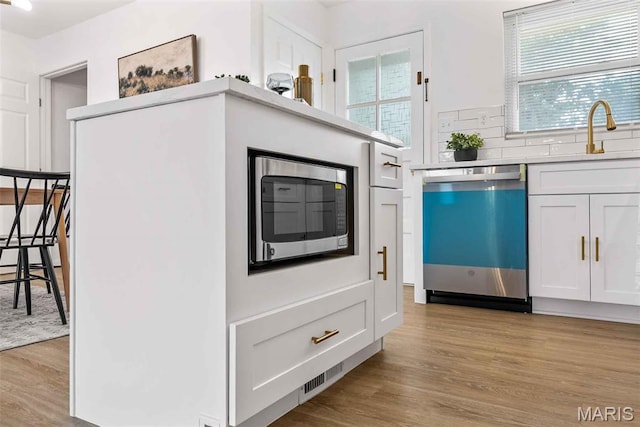 216 Clearpoint Ln, Saint Louis, MO 63123 - kitchen with stainless steel appliances, a sink, light wood-style flooring, white cabinets, and light countertops