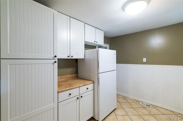 8217 Buchanan Ave, Saint Louis, MO 63114 - kitchen with freestanding refrigerator, white cabinets, wainscoting, light tile patterned floors, and light countertops