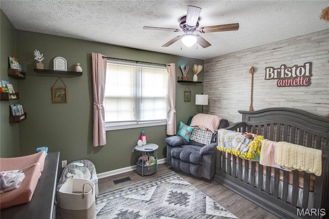 906 E Fairgrounds Ave, Jerseyville, IL 62052 - bedroom featuring a textured ceiling, a crib, wooden walls, ceiling fan, and wood finished floors
