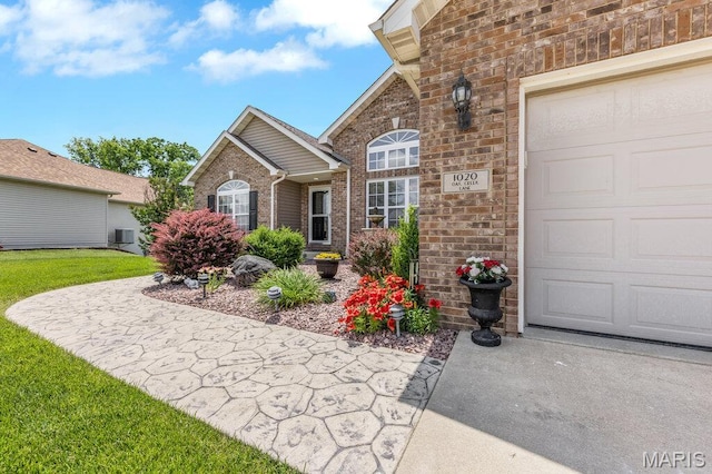 1020 Oak Creek Ln, Waterloo, IL 62298 - view of exterior entry featuring brick siding, a garage, central air condition unit, and a lawn