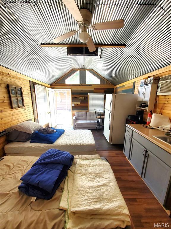 303 Arrowhead Trl, Hermann, MO 65041 - bedroom with wood walls, freestanding refrigerator, a sink, vaulted ceiling, and dark wood-type flooring