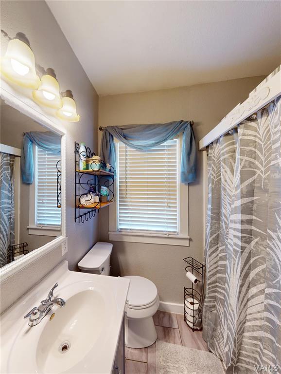 604 N Hena St, Greenville, IL 62246 - bathroom with vanity, toilet, wood finished floors, a shower with shower curtain, and baseboards