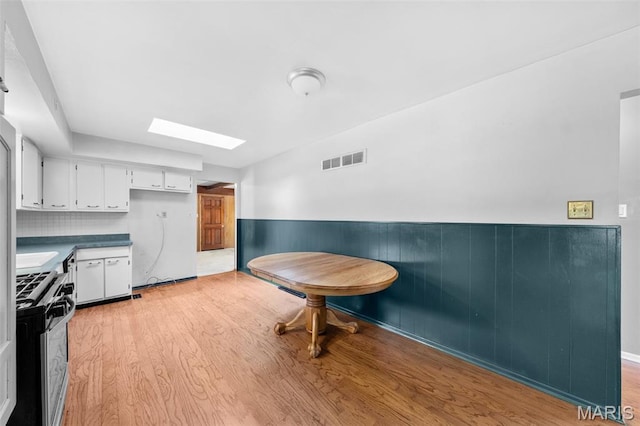 417 Concordia Ln, Saint Charles, MO 63301 - kitchen featuring stainless steel range with gas cooktop, a skylight, white cabinets, light wood-type flooring, and a wainscoted wall