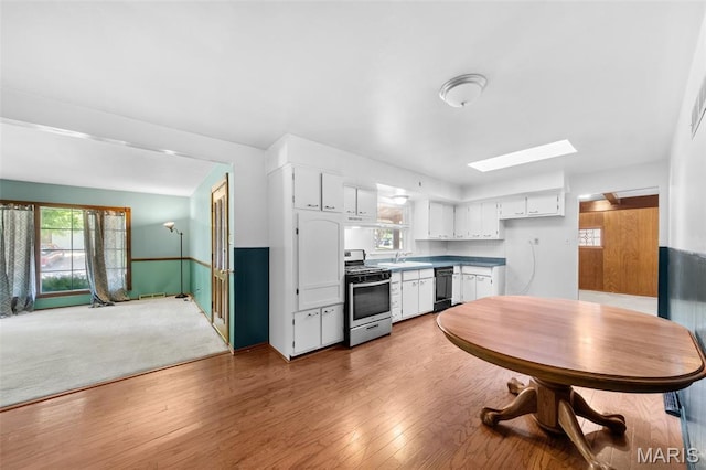 417 Concordia Ln, Saint Charles, MO 63301 - kitchen featuring stainless steel gas range oven, dishwasher, a skylight, white cabinets, and light wood-style floors