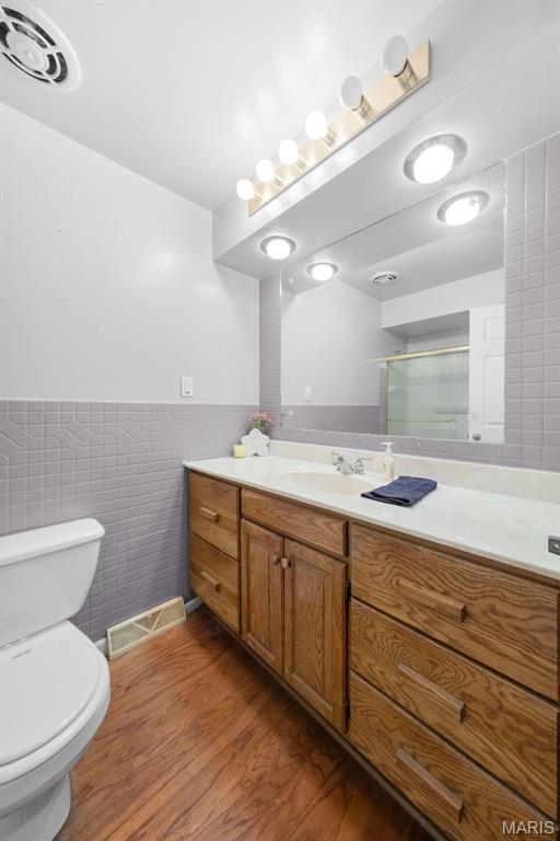 417 Concordia Ln, Saint Charles, MO 63301 - bathroom featuring tile walls, vanity, wood finished floors, an enclosed shower, and wainscoting