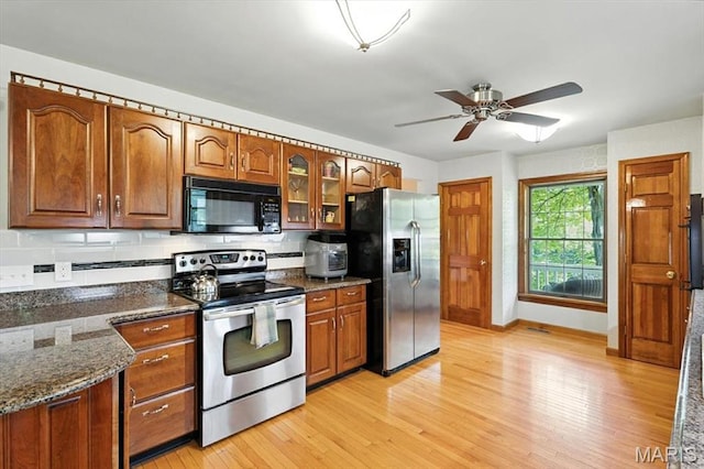 18232 Prickly Pear Ct, Pacific, MO 63069 - kitchen with appliances with stainless steel finishes, light wood-type flooring, a ceiling fan, brown cabinetry, and dark stone countertops