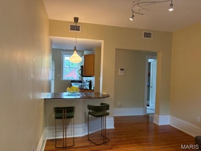 6114 Washington Blvd Unit 302, Saint Louis, MO 63112 - kitchen featuring wood finished floors, a peninsula, baseboards, decorative light fixtures, and a kitchen breakfast bar