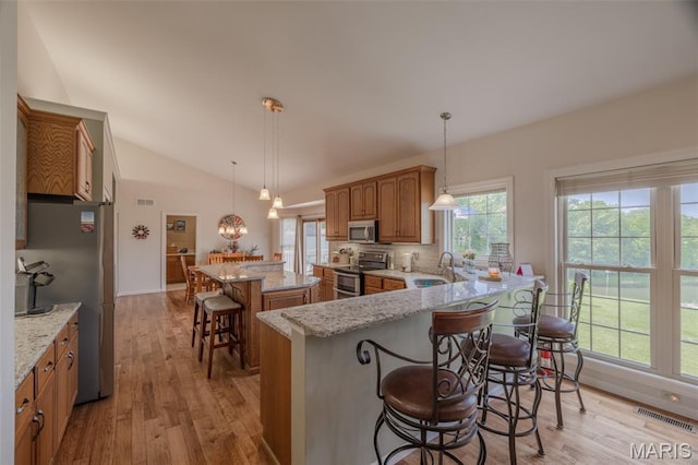 11400 Macs Cove Dr, Wright City, MO 63390 - kitchen with stainless steel appliances, a breakfast bar area, brown cabinetry, a center island, and vaulted ceiling