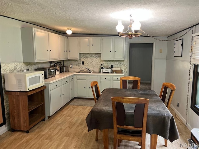 11142 E State Highway 47, Cadet, MO 63630 - kitchen featuring white microwave, a chandelier, light wood-style flooring, decorative backsplash, and light countertops