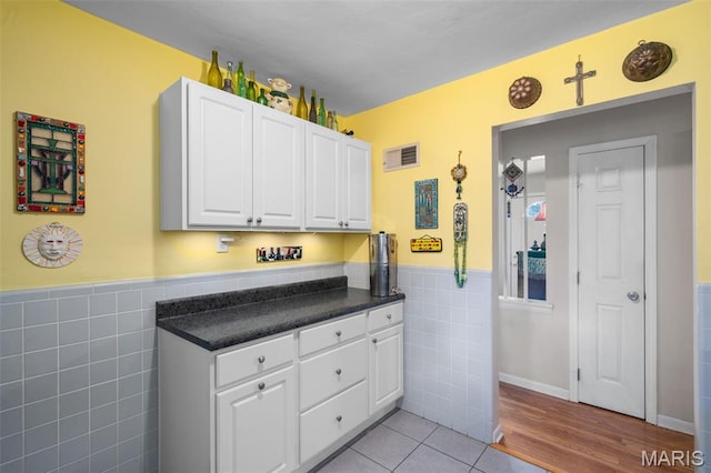2604 Jonathan Dr, Mehlville, MO 63125 - kitchen featuring tile walls, white cabinetry, wainscoting, light tile patterned floors, and dark countertops