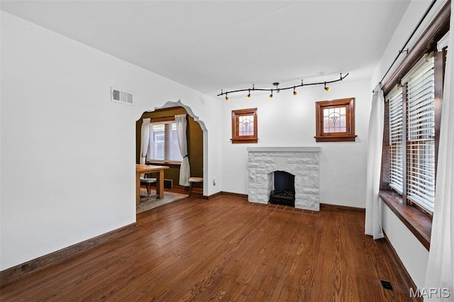 6314 Chippewa St, Saint Louis, MO 63109 - unfurnished living room with a stone fireplace, wood finished floors, arched walkways, baseboards, and track lighting