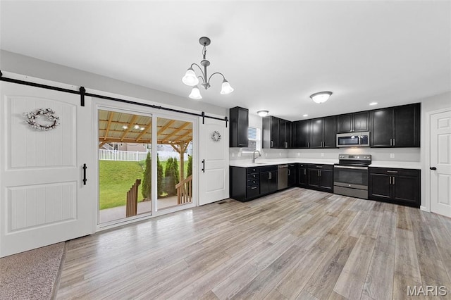 3169 Willow Point Dr, Imperial, MO 63052 - kitchen with appliances with stainless steel finishes, a barn door, dark cabinets, light countertops, and light wood-style flooring