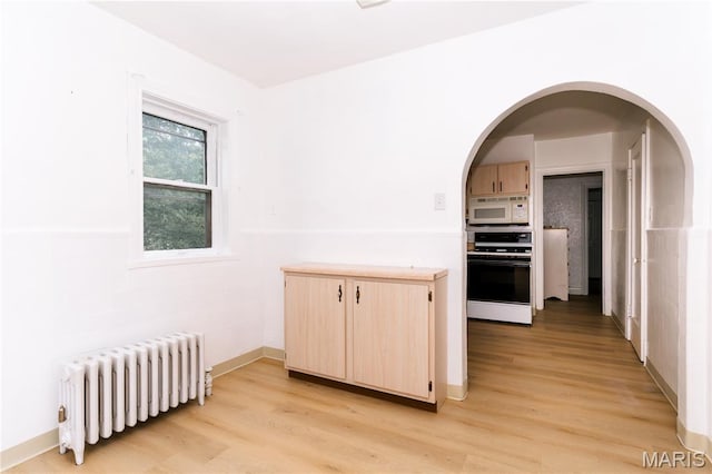 7360 Dartmouth Ave, University City, MO 63130 - kitchen with radiator heating unit, stove, white microwave, light brown cabinetry, and light wood-style floors