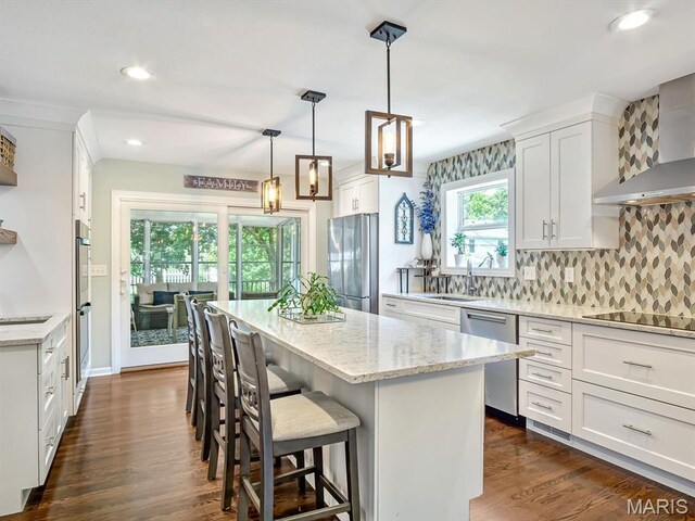 201 Banner St, Edwardsville, IL 62025 - kitchen featuring appliances with stainless steel finishes, wall chimney exhaust hood, a kitchen island, backsplash, and white cabinetry