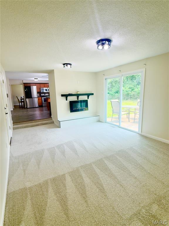 11630 Carolview Dr, Florissant, MO 63033 - unfurnished living room with light colored carpet, a textured ceiling, baseboards, and a glass covered fireplace