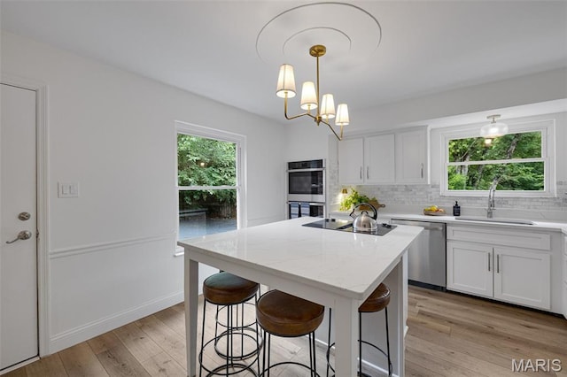 173 Portico Dr, Chesterfield, MO 63017 - kitchen featuring appliances with stainless steel finishes, a sink, a kitchen island, backsplash, and light wood-style floors
