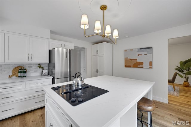 173 Portico Dr, Chesterfield, MO 63017 - kitchen with freestanding refrigerator, black electric stovetop, white cabinetry, light wood-style floors, and backsplash