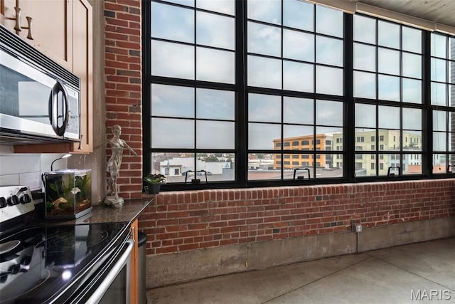 2323 Locust St Unit 308, Saint Louis, MO 63103 - kitchen featuring appliances with stainless steel finishes, brick wall, dark countertops, healthy amount of natural light, and concrete flooring