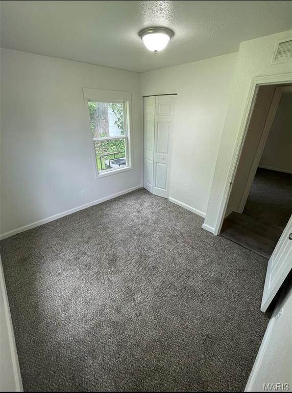 unfurnished bedroom featuring a closet, dark colored carpet, and a textured ceiling