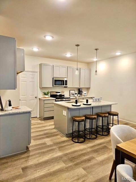 3063 Pirogue St, Saint Charles, MO 63301 - kitchen with appliances with stainless steel finishes, light wood-style floors, gray cabinetry, a breakfast bar area, and pendant lighting