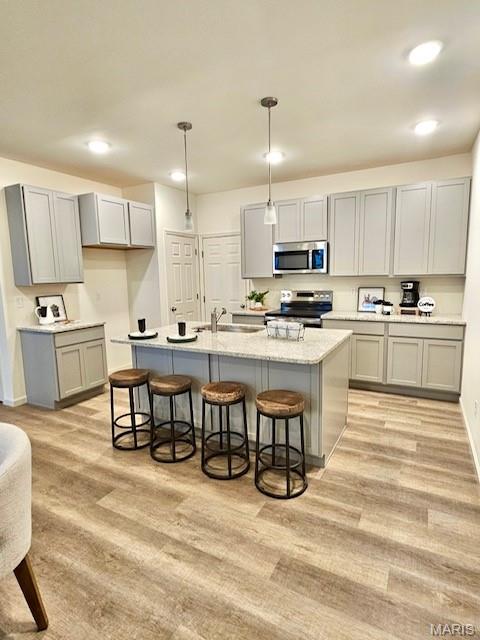 3063 Pirogue St, Saint Charles, MO 63301 - kitchen featuring stainless steel appliances, gray cabinets, a kitchen bar, light wood-style floors, and a kitchen island with sink