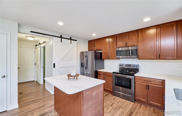 2907 Preston Woods Trl, Lake St Louis, MO 63367 - kitchen featuring appliances with stainless steel finishes, a barn door, light wood-style flooring, a center island, and backsplash