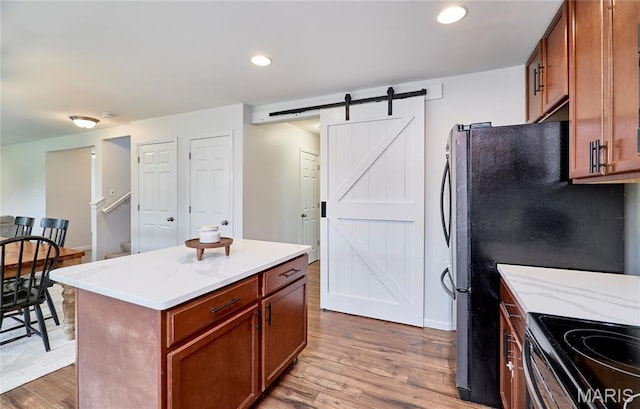 2907 Preston Woods Trl, Lake St Louis, MO 63367 - kitchen with a barn door, wood finished floors, a center island, brown cabinetry, and light stone countertops
